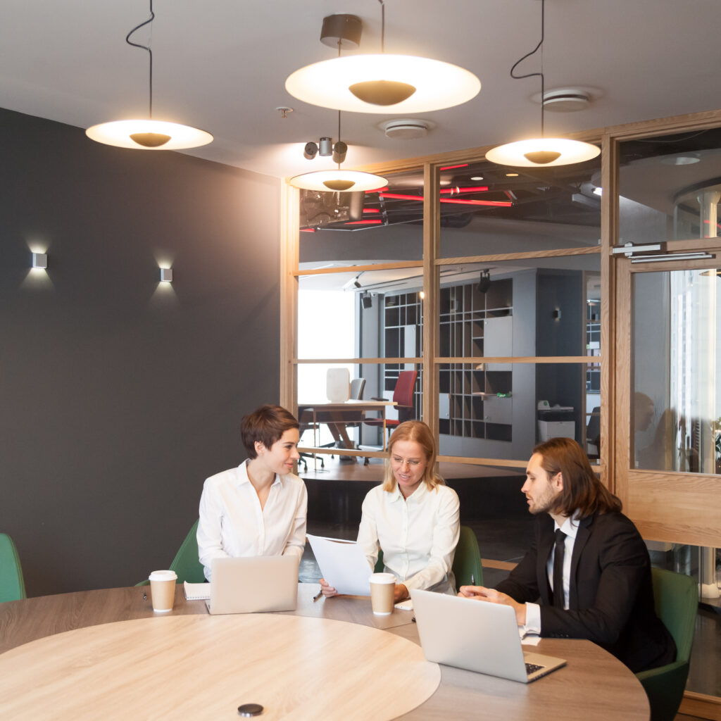 Businesspeople talking using laptops at corporate team meeting in modern office interior, colleagues discussing document or planning project at group negotiations working together in conference room